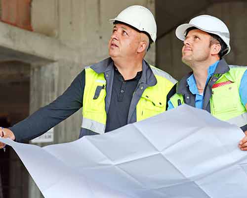 Two construction managers on a building site holding construction planning documents
